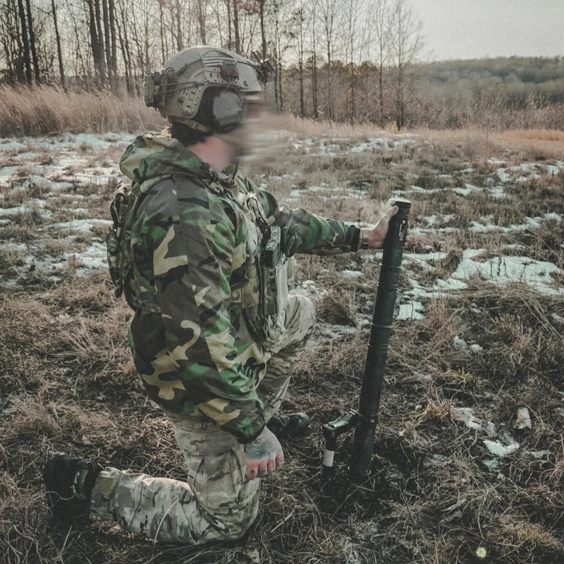 Person in camouflage gear using a device in a forested area