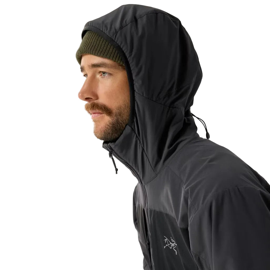 Image showing the Arc'teryx PRO Practitioner AR Hoody in Carbon Copy with the ScubaHood in use, highlighting the helmet compatible design, weather resistant Fortius Air 50 fabric, and operator focused performance ideal for tactical work and alpine environments across the United States.