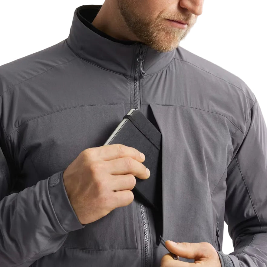 Arc'teryx PRO Practitioner AR Jacket in Wolf Grey shown being worn while accessing the front chest pocket. Demonstrates how the PRO-series mid layer allows quick, quiet access to mission essentials with its Fortius Air 50 shell and low-bulk Octa Loft insulation. Ideal for anyone searching for a breathable tactical mid layer with secure storage for field gear, comms, notebooks, or ID in military, law enforcement, or backcountry environments.