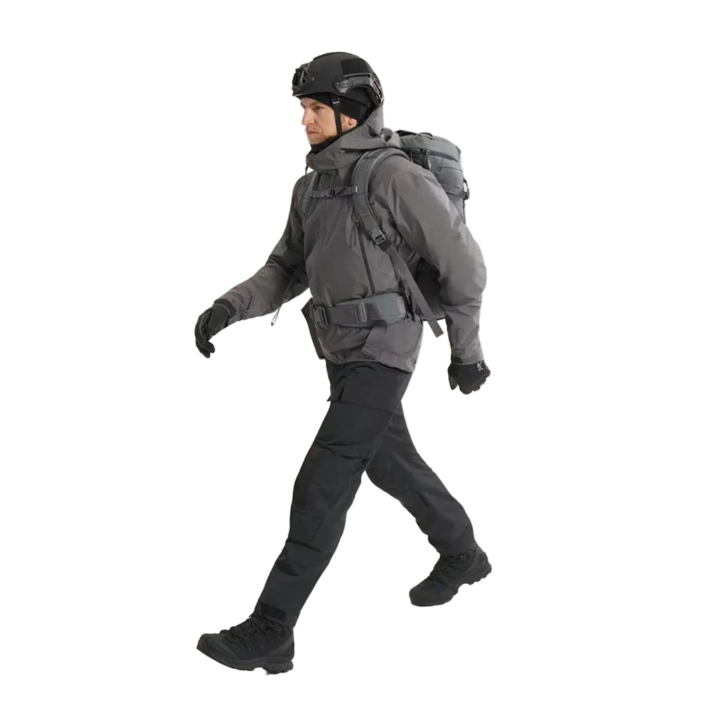 Full body view of the Arc'teryx PRO Practitioner AR Jacket in Wolf Grey being worn with a tactical backpack and load-bearing kit. Highlights how the PRO-series mid layer integrates under gear thanks to its Fortius Air 50 breathable shell and low-bulk Octa Loft insulation. Ideal for users searching how the Practitioner AR performs in real operational setups, under packs, with armor, or in high-mobility field environments.