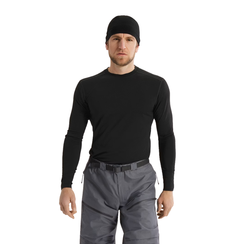 A man wearing a black long-sleeve performance base layer shirt, black beanie, and gray pants, standing against a plain white background.