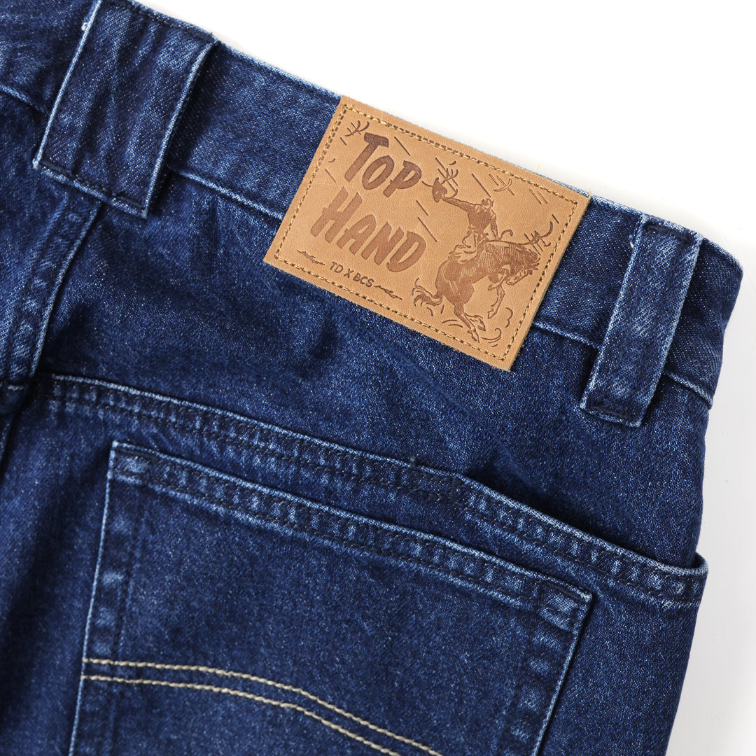Close-up of blue jeans with a 'Top Hand' leather label on a white background