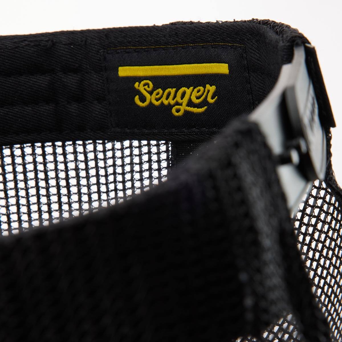 Close-up of a black mesh hat with 'Seager' logo in yellow on a white background