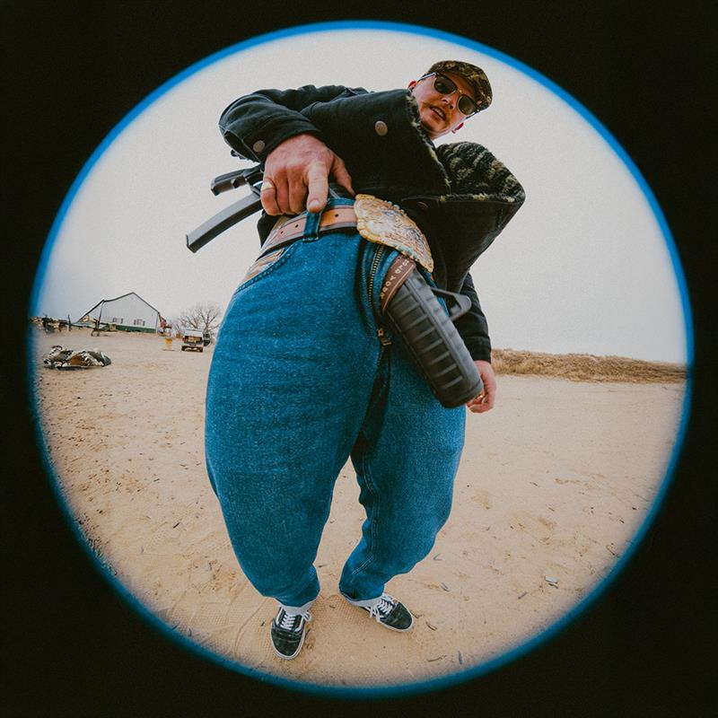 Person holding a rifle in an open field with a building in the background
