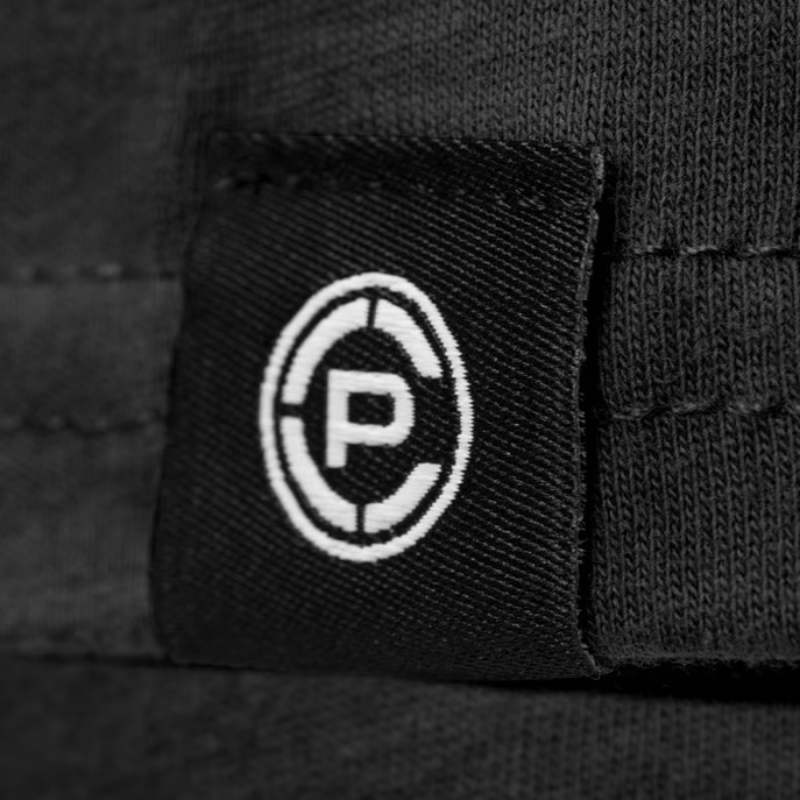 Close-up of a black fabric patch with a white circular logo containing a stylized letter CP, attached to a black woven textile surface.