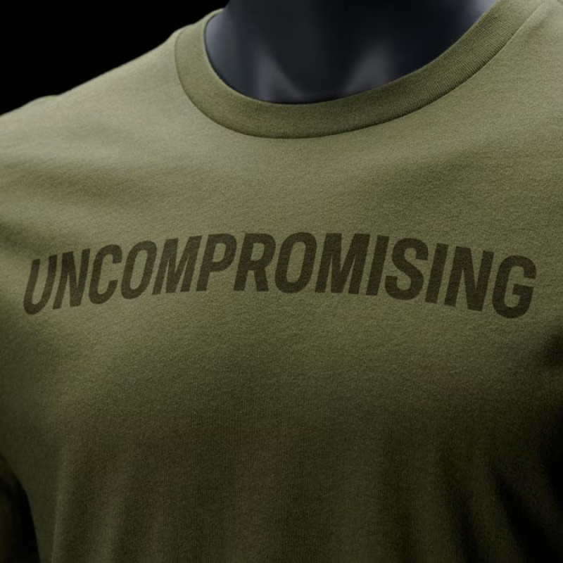 Close-up of an olive green crewneck t-shirt displayed on a dark mannequin torso, featuring the word 'UNCOMPROMISING' printed across the chest in a dark brown font.