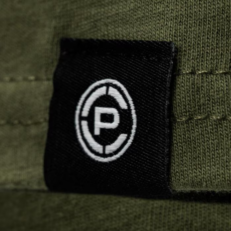 Close-up of a black fabric patch with a white circular 'CP' logo, sewn onto an olive green ribbed textile surface.