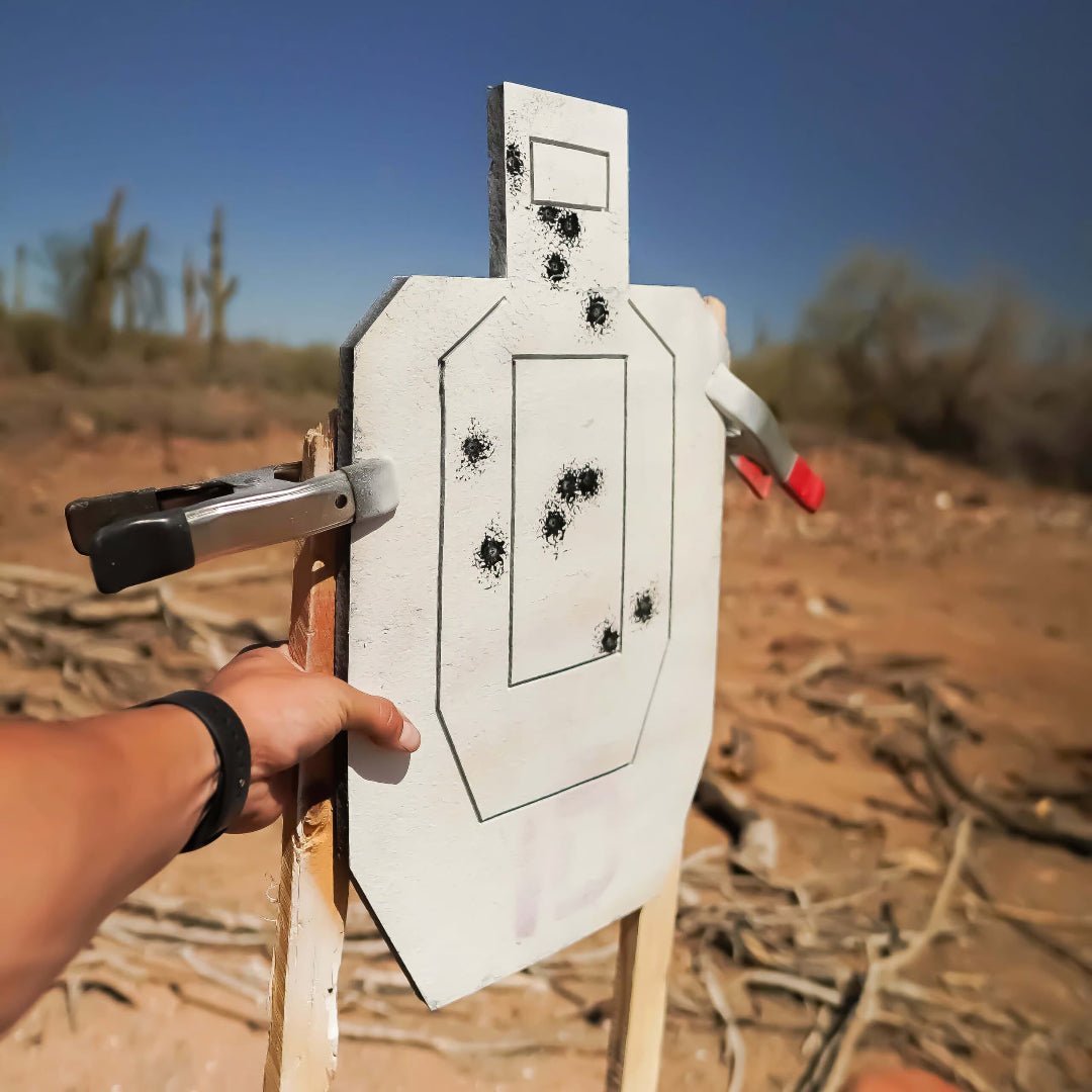 Target with bullet holes held by a person in an outdoor setting