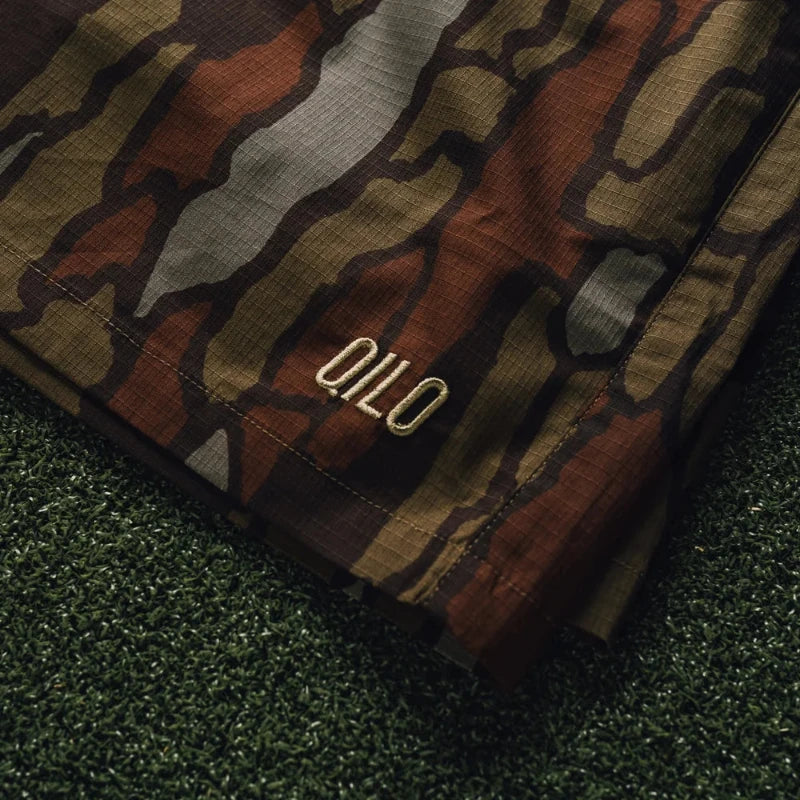 Trebark Camouflage-patterned fabric with 'QILO' branding on a grassy background
