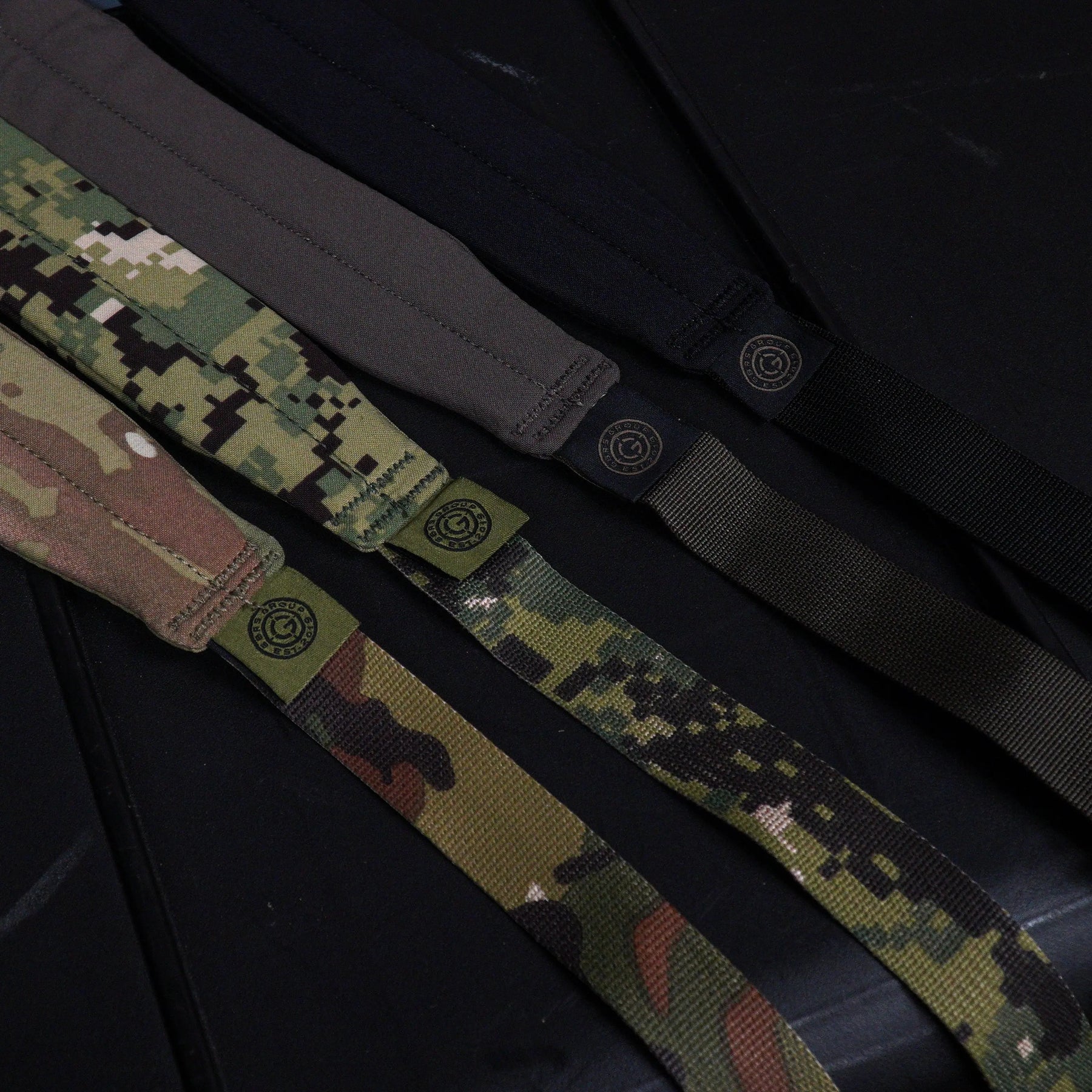 Multiple GBRS Group SBS Slings in assorted colorways laid out on a rifle case, lightweight minimalist adjustable tactical rifle slings with padded neck sections and low profile webbing for professional weapon setups made in the USA