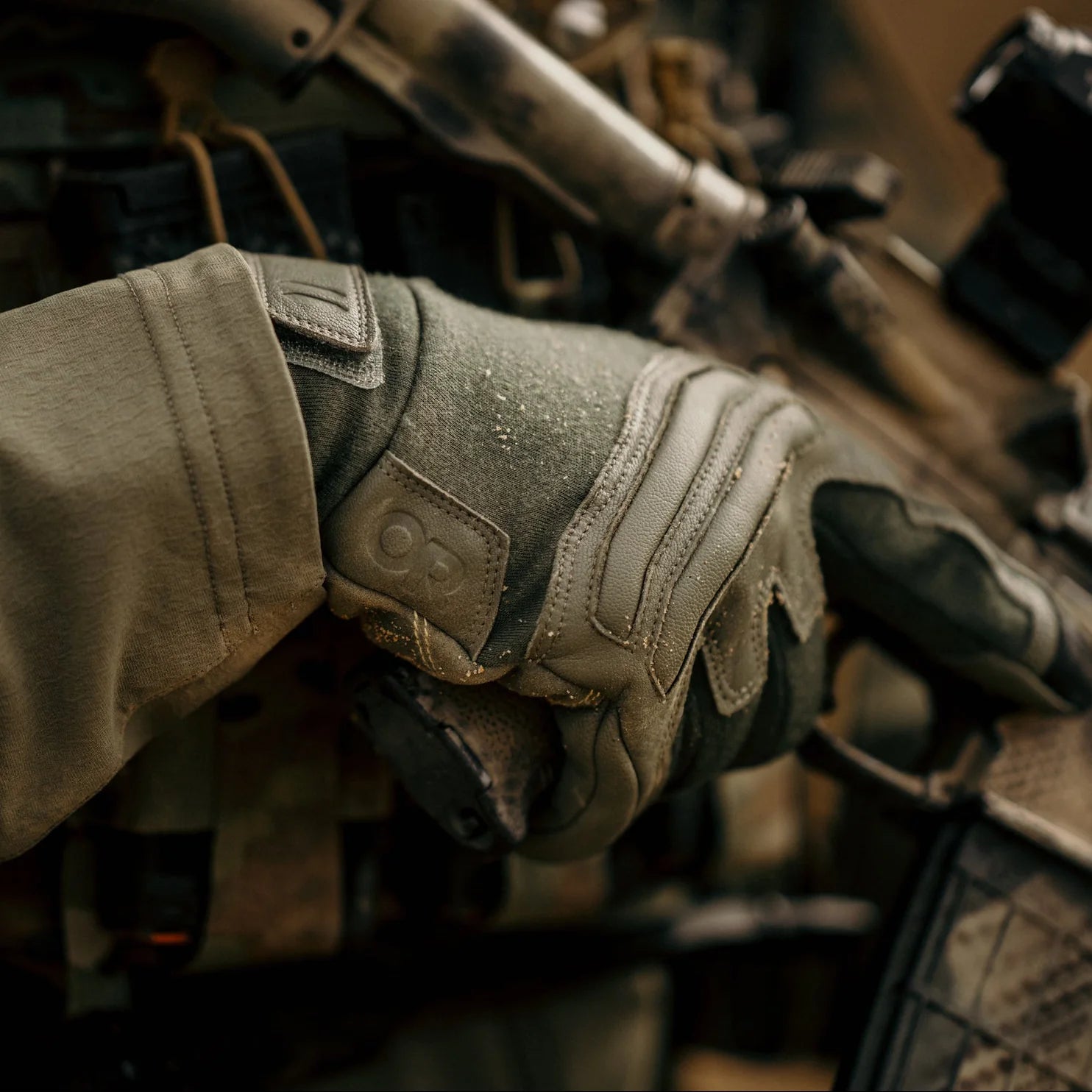 Operator wearing Outdoor Research Ironsight II FR Gloves in Ranger Green during field operations, flame resistant Nomex and Kevlar tactical duty gloves integrated into combat gear setup for military missions, range training, and law enforcement duty applications