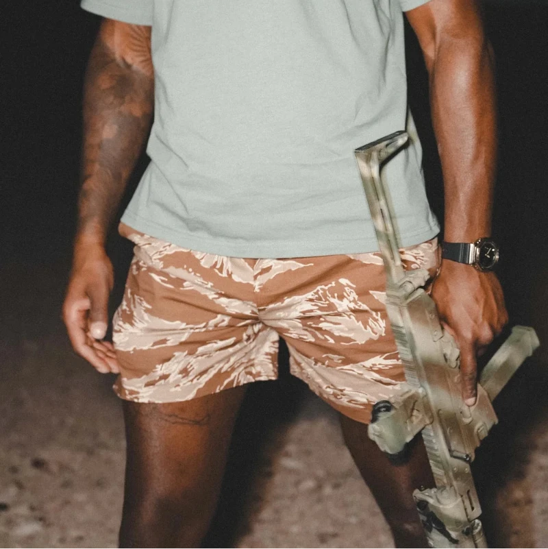 Person wearing a light green t-shirt with a graphic design and Tiger stripe patterned shorts outdoors.