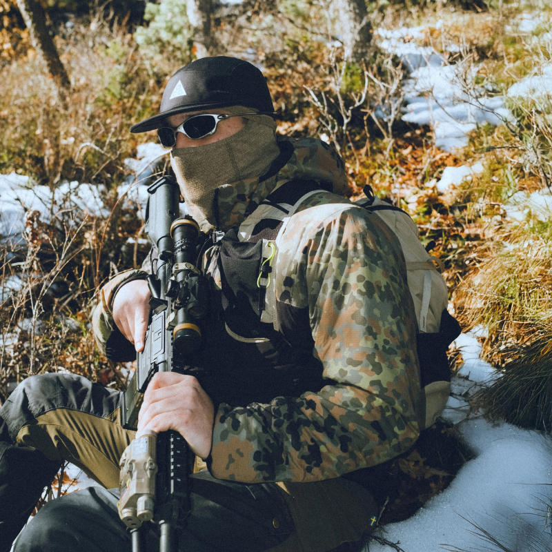 Lifestyle image of a user wearing the Qilo Ostwind Insulated Mid Layer Jacket in snowy conditions, showing the athletic fit, insulated warmth, and weather resistant shell while handling tactical equipment. Shot in a cold weather field environment to highlight real world performance. Available from Tactical Distributors for U.S. tactical and outdoor users.