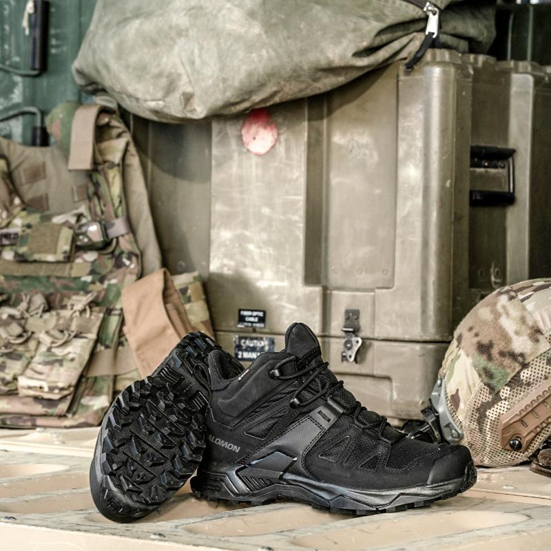 Pair of Salomon FORCES X Ultra Mid boots in Black staged in a military environment showing the tactical lightweight design, Advanced Chassis stability, and All Terrain Contagrip traction built for military operations, law enforcement missions, mountain trekking, and rugged field use.