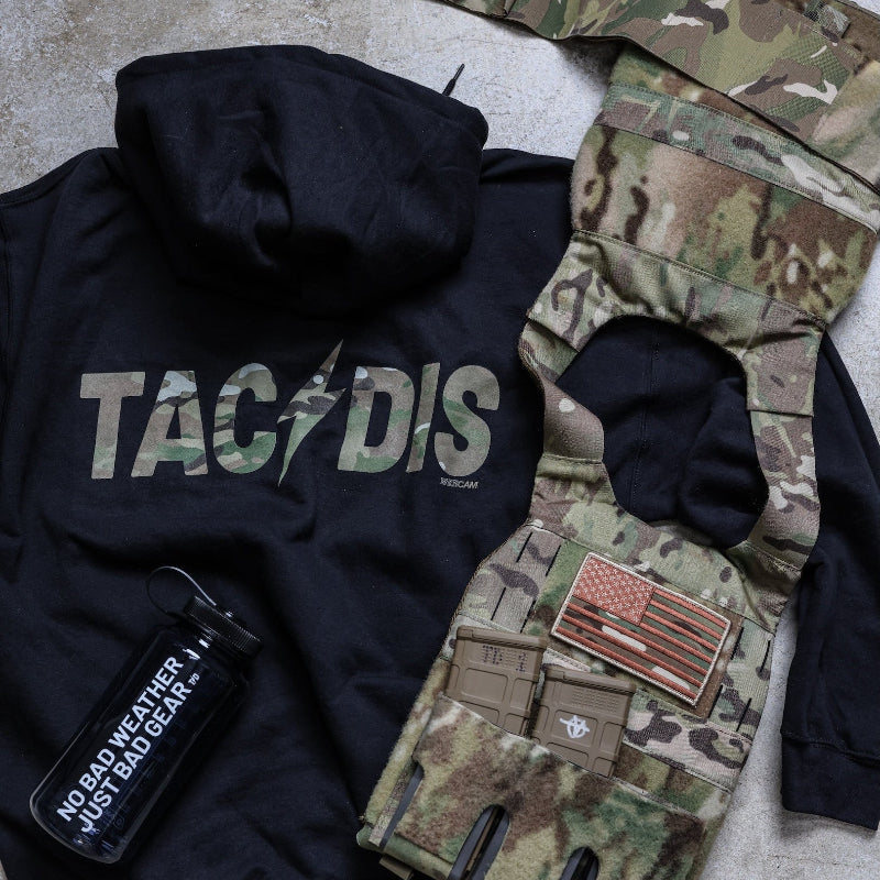Black hoodie with 'TAC/DIS' text, camouflage jacket, and tactical pouch on a concrete surface.