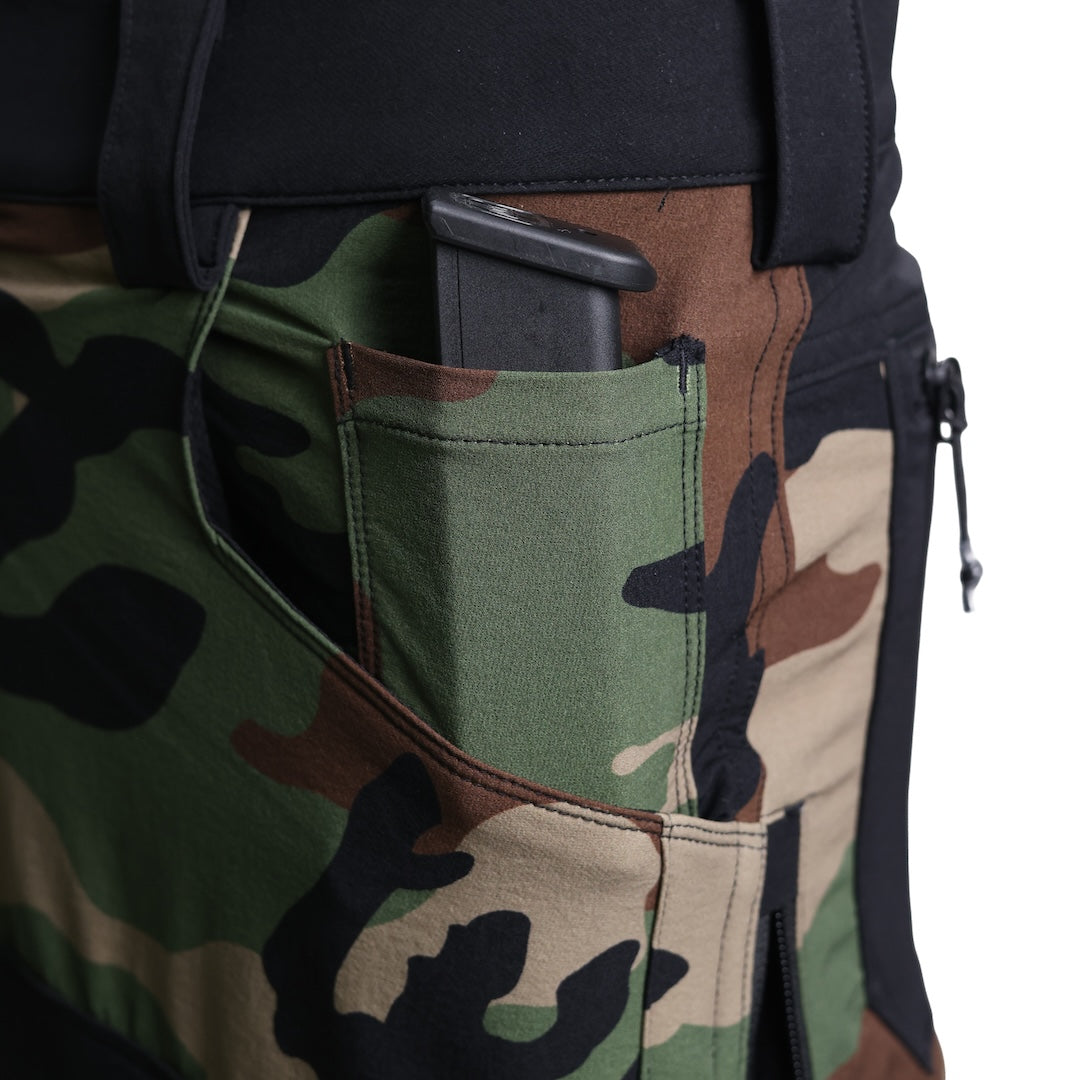 Close-up of the TD Cordell Combat Pants V2 in the Colorblocked M81 Woodland and Black version showing a magazine inserted into the small interior front pocket. Highlights the discreet mag-sized pocket designed for fast access, reinforced stitching, and rugged softshell construction. Ideal for users searching for tactical pants with interior mag pockets, M81 Woodland EDC trousers, or colorblocked combat pants optimized for range reloads and field-ready carry setups.