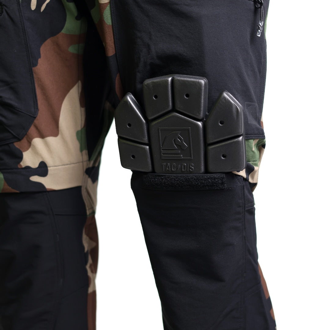 Close-up of the TD Cordell Combat Pants V2 in the Colorblocked M81 Woodland and Black version showing a knee pad being inserted into the dedicated knee pad pocket. Highlights the reinforced knee panel construction, ergonomic articulation, and compatibility with impact-resistant knee inserts. Ideal for users searching for M81 Woodland combat pants with knee pad integration, colorblocked tactical pants with modular protection, and field-ready EDC trousers designed for mobility and durability.
