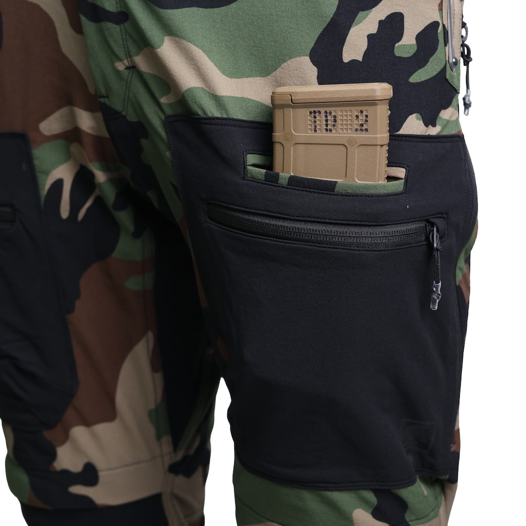Close-up of the TD Cordell Combat Pants V2 in the Colorblocked M81 Woodland and Black version with an AR magazine inserted into the side mag pocket. Shows the secure welted pocket design, reinforced construction, and fast-access placement ideal for reloads. Perfect for users searching for M81 Woodland tactical pants with AR mag pockets, colorblocked combat pants with EDC storage, or range-ready trousers built for high-mobility shooting environments.