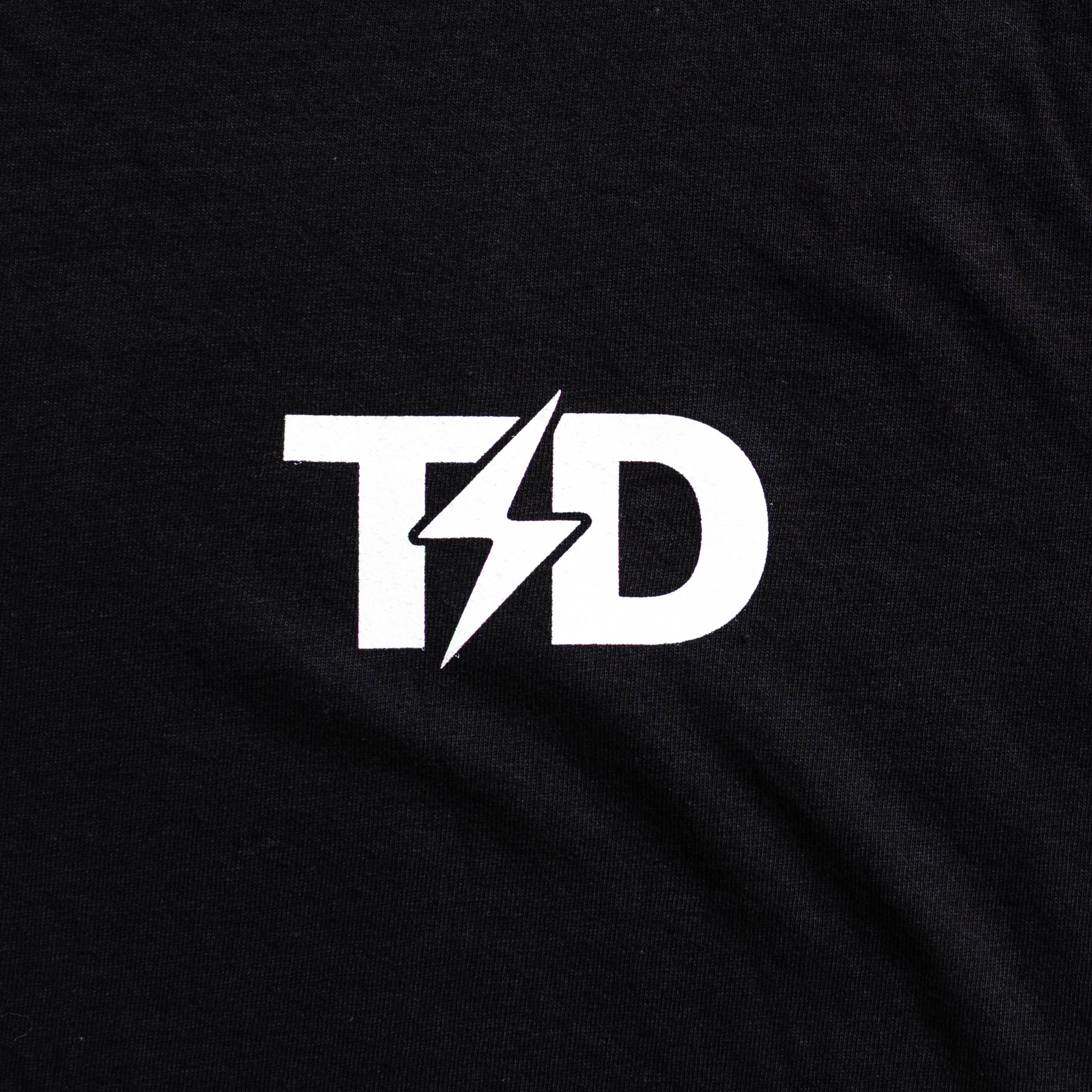Close-up of the front graphic on the TD Lip Pillow Tee. Featuring a clean, classic design with the subtle TAC DIS logo, this nicotine pouch inspired shirt combines comfort and style with a nod to off-duty freedom. Made from heavyweight cotton for all-day wear.