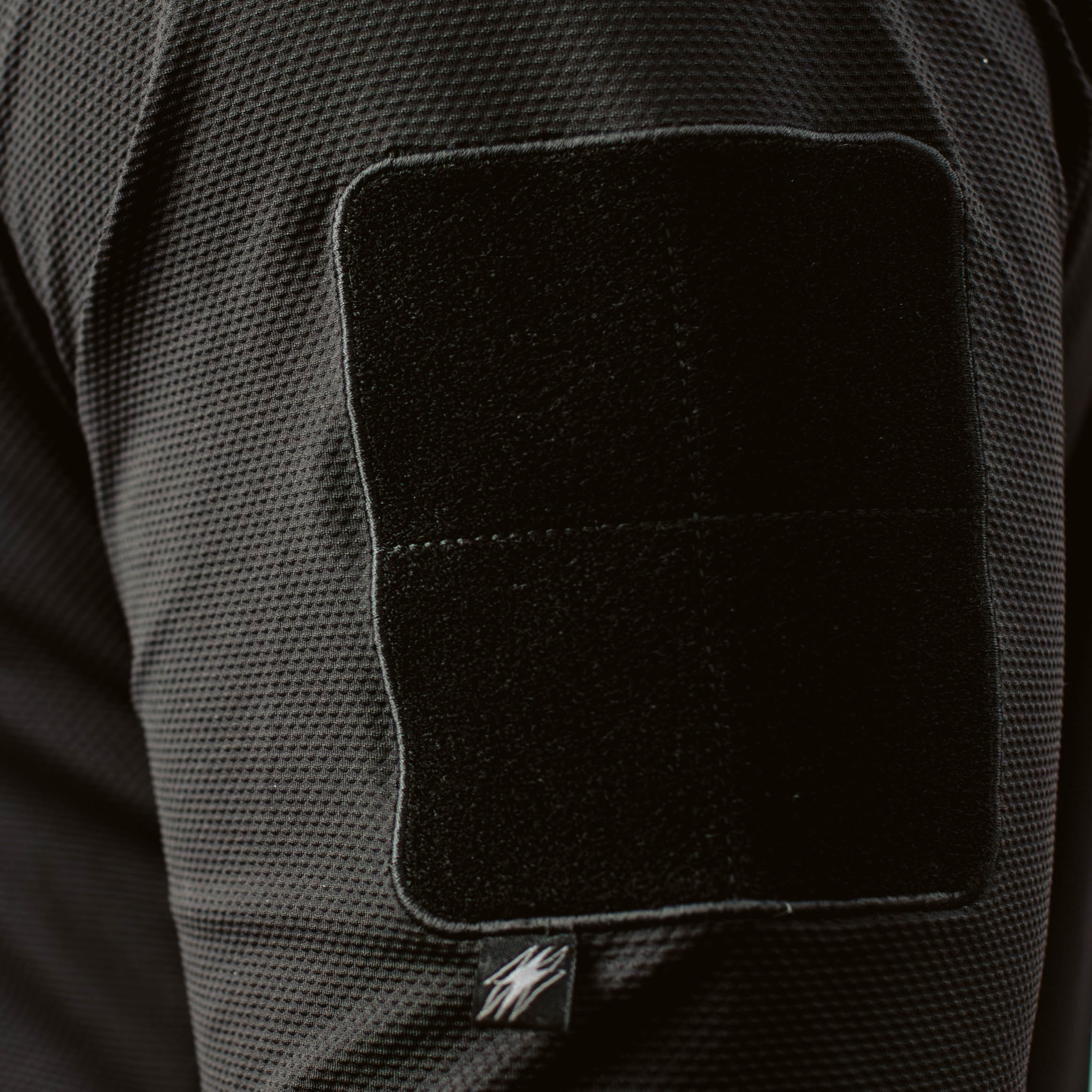Close up of TD OSS Top V2 Long Sleeve in Black showing low profile tricot loop patch field on bicep, streamlined tactical combat base layer operator top built for shooter setups, range training, and duty use under plate carriers