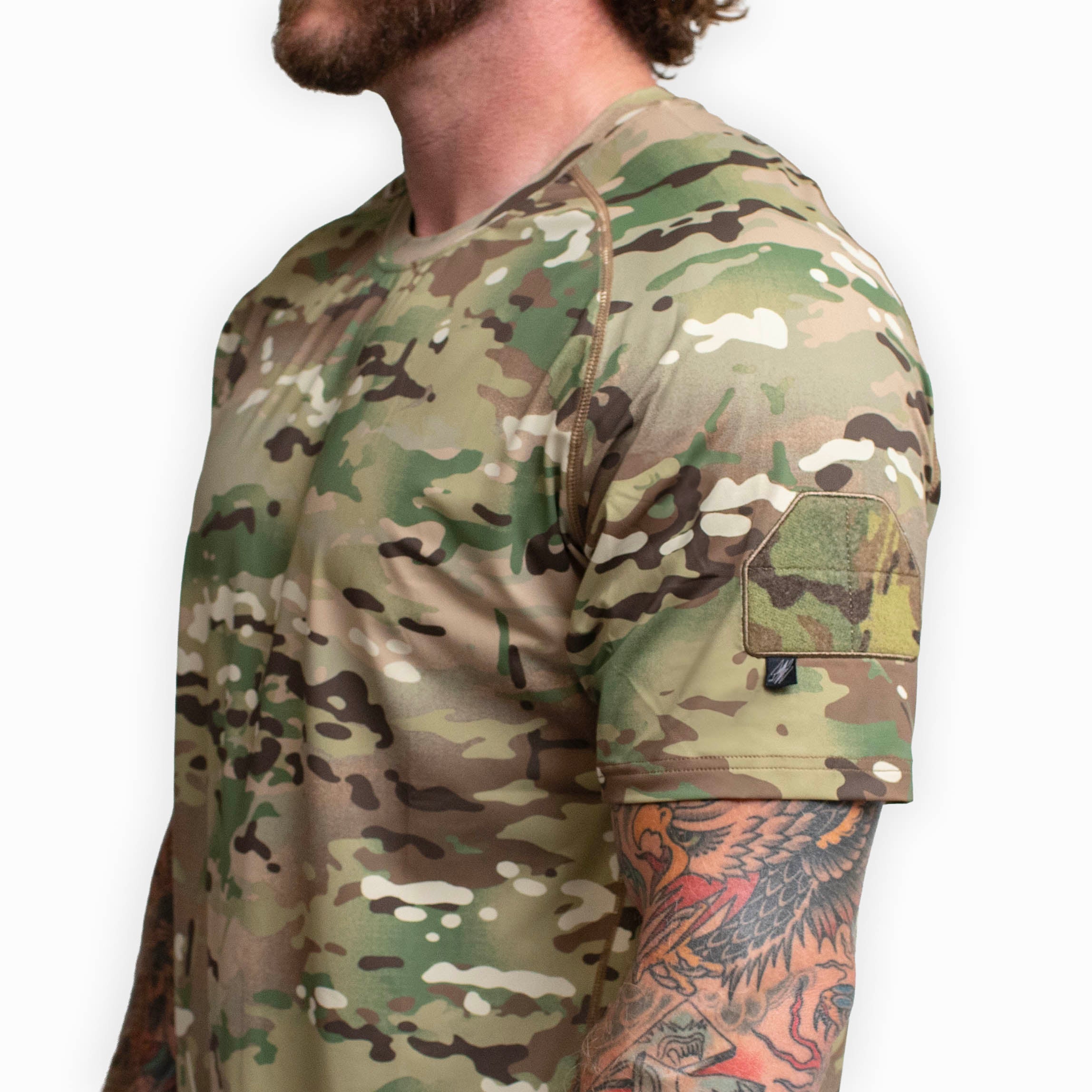 Close up detail of the TD Shooter Shirt MultiCam short sleeve showing the MIL SPEC MultiCam loop bicep patch, tonal flatlock stitching, and durable 4 way stretch performance fabric used for tactical training and range work. Image optimized for Tactical Distributors customers across the United States.