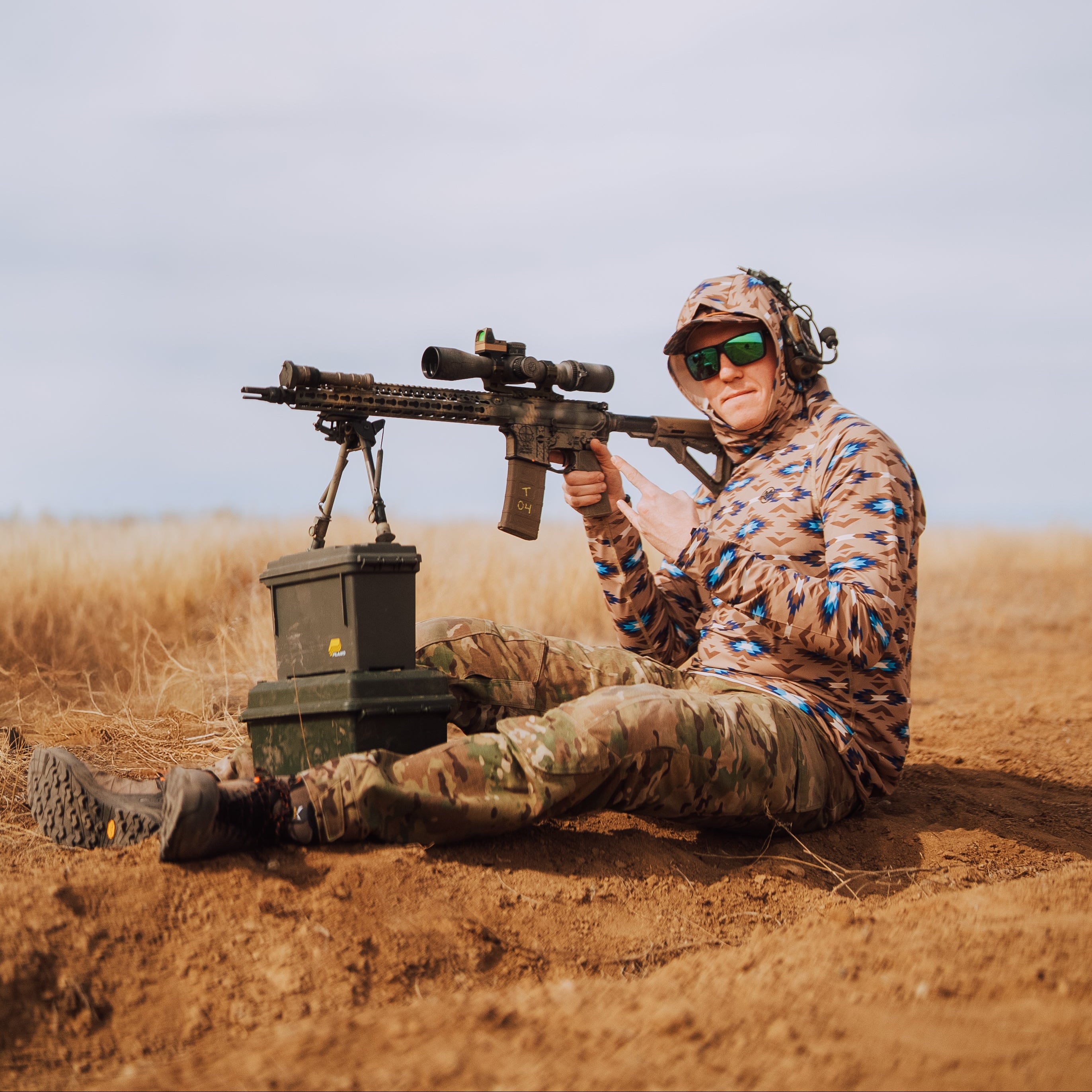 TD x Black Canyon Systems Southwest Tan tactical sun hoodie worn while seated during range day break, breathable hot weather shooting shirt with moisture wicking fabric and UV protection built for all day outdoor training sessions