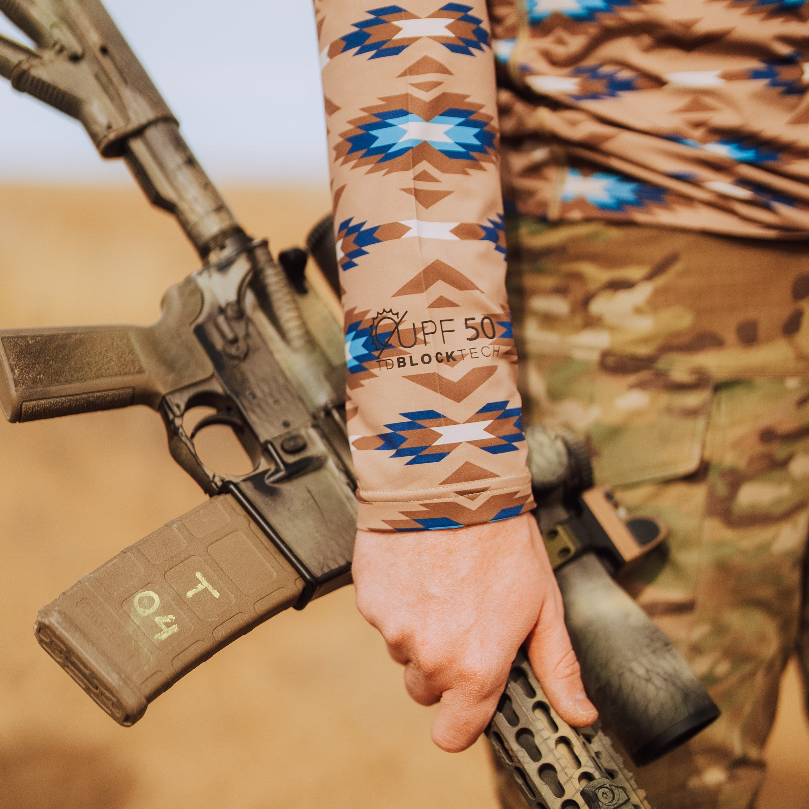 Close up of TD x Black Canyon Systems Southwest Tan sun shirt sleeve highlighting UPF 50 TD Blocktech sun protection marking, lightweight stretch performance fabric engineered for UV defense during desert range training and outdoor exposure