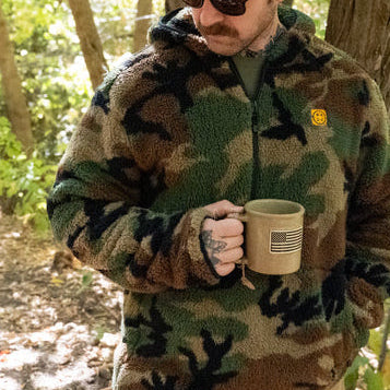Man wearing the TD x Black Rifle Coffee Co. Reticle Half-Zip Fleece in woodland camo, showing relaxed fit and high-pile Sherpa fleece warmth. Tactical pullover built for cold-weather comfort with breathable mesh trim and co-branded TD x BRCC detailing. Perfect for range days, coffee runs, and off-duty missions.