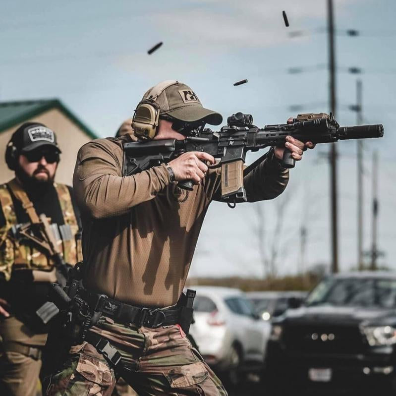 Lifestyle image of the Velocity Systems BOSS Rugby Long Sleeve Combat Shirt worn while shooting, highlighting its athletic fit, breathable 4-way stretch nylon-spandex fabric, and sling-friendly low-profile collar. Built for tactical shooters, law enforcement, and military operators, this combat base layer provides unrestricted movement, moisture-wicking comfort, and durable performance during firearms training, live range drills, and dynamic shooting scenarios. Made in the USA and available at Tac Dis.