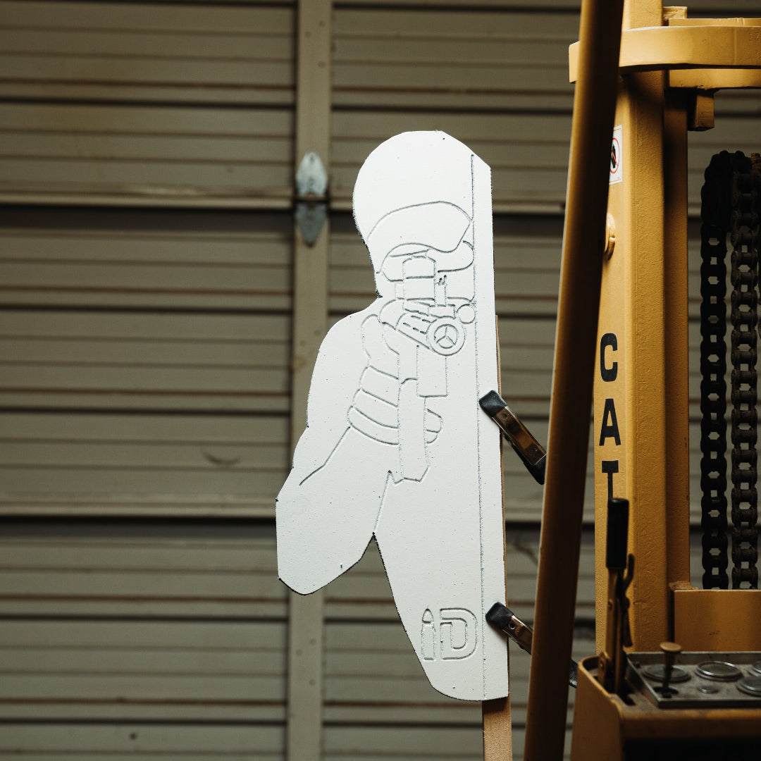 White silhouette of a target against a metallic background, next to a yellow piece of machinery.