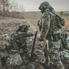 Two soldiers in camouflage gear working together in a field.