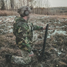 Person in camouflage gear using a device in a forested area