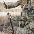 Person in camouflage gear holding a rocket launcher in an outdoor setting