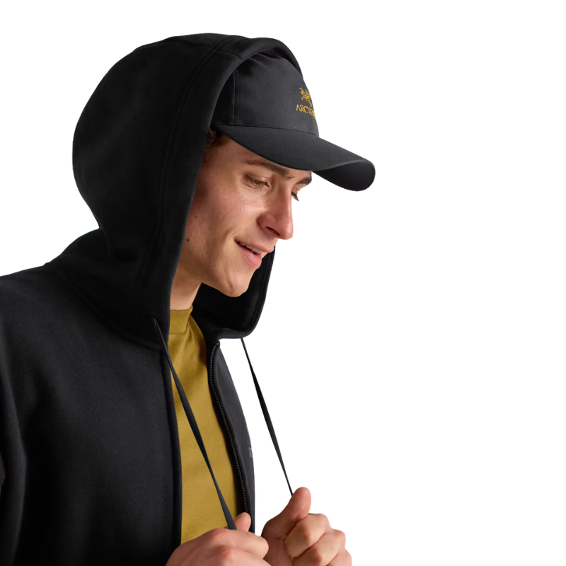A man wearing a black zip-up hoodie with a built-in hood and a matching black baseball cap with a small yellow Arc'teryx logo, shown against a plain white background.