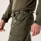 Close-up of a person wearing ranger green tactical cargo pants with a matching belt, shown from the waist down against a light neutral studio background.