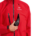 Close view of the Arc'teryx Alpine Guide Jacket in Dynasty II red showing the front pocket in use with a radio for professional ski guide communication and GORE TEX PRO winter protection featured in the Arc'teryx on sale collection.