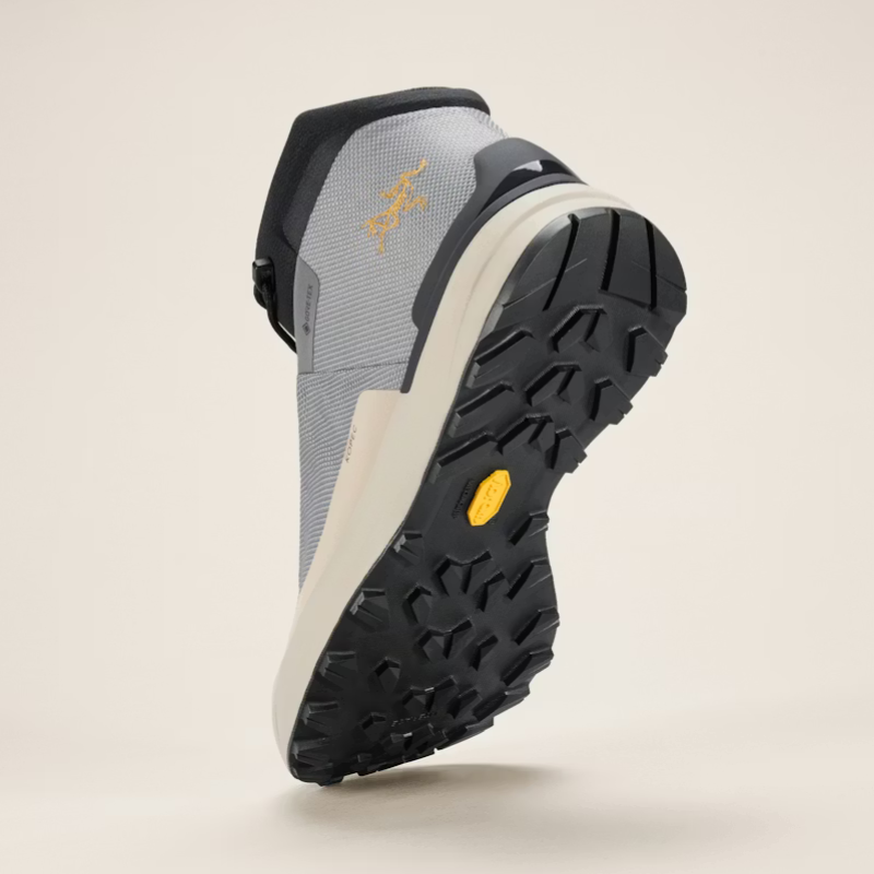 Gray hiking boot with black sole and yellow Arc'teryx logo on a beige background