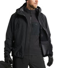Detail view of the Arc'teryx PRO Alpha LT Jacket Gen 2.2 in Black worn open as a lightweight GORE TEX shell layered over another jacket, highlighting its military fit, weatherproof construction, and low profile design evolved from the Arc'teryx LEAF program. Shows how the PRO Alpha LT functions as an outer layer in wet weather tactical environments.