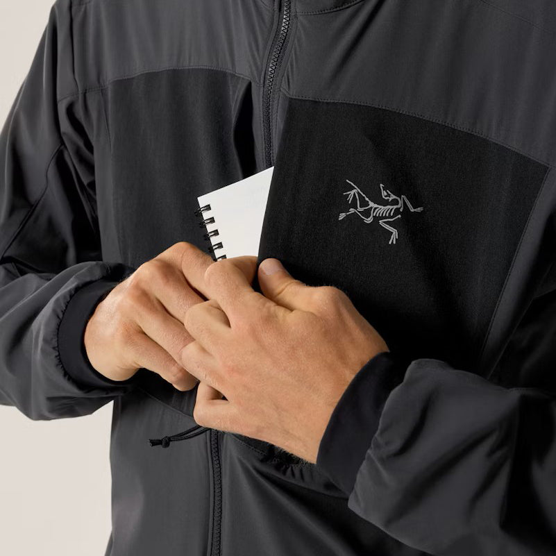 Image showing the Arc'teryx PRO Practitioner AR Hoody in Carbon Copy with a hand accessing the front zip pocket demonstrating the dual chest storage design, streamlined access points, and mission ready pocket placement for tactical and alpine use.