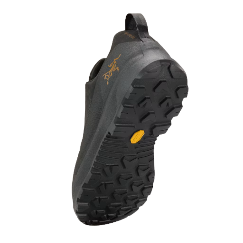 A single black slip-on shoe shown from the side, featuring a rugged treaded sole, a small yellow Vibram accent on the midsole, and a gold Arc'teryx logo on the side.