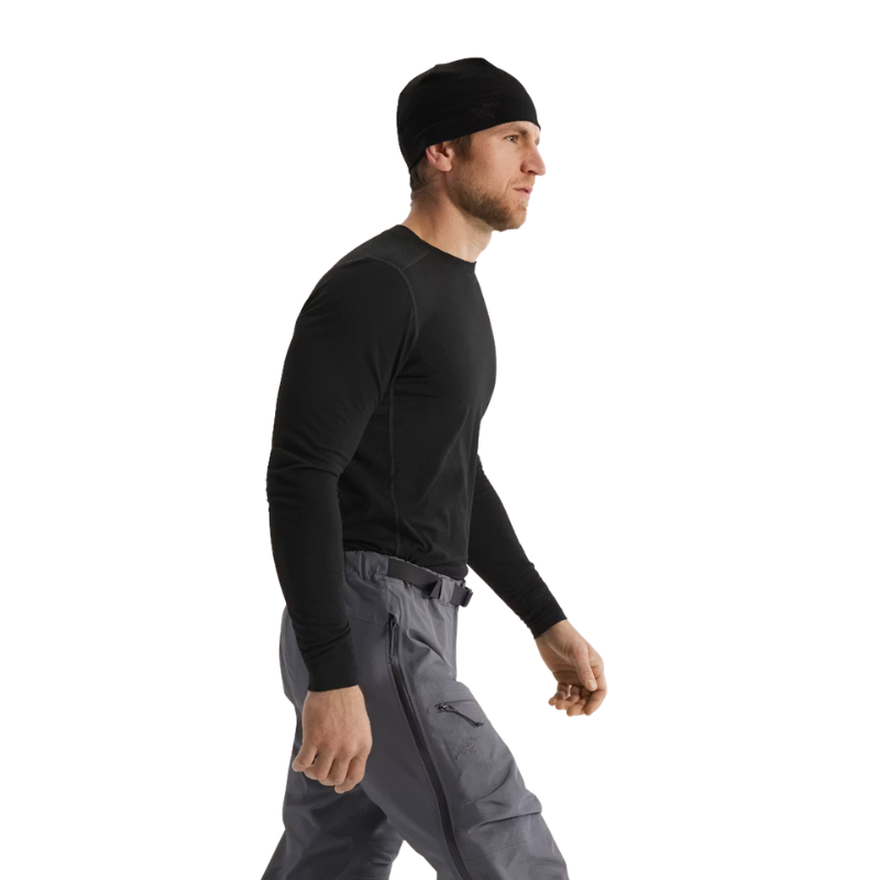 A man in profile wearing a black long-sleeve performance shirt, gray cargo pants, and a black beanie, photographed against a solid white background.
