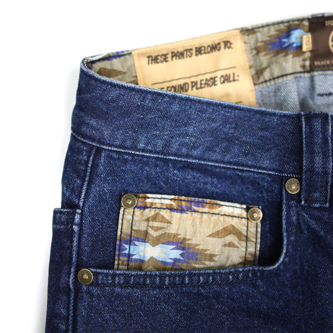 Close-up of blue jeans with a patterned patch and label on a white background