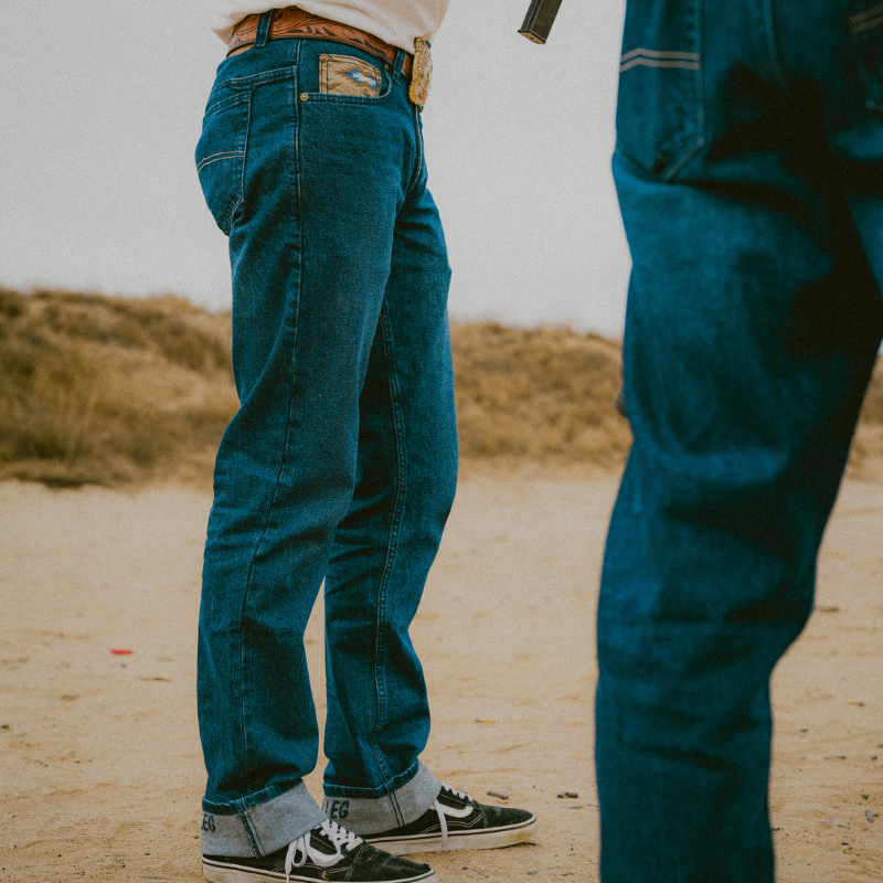 Two people wearing blue jeans standing on a sandy surface with a blurred background