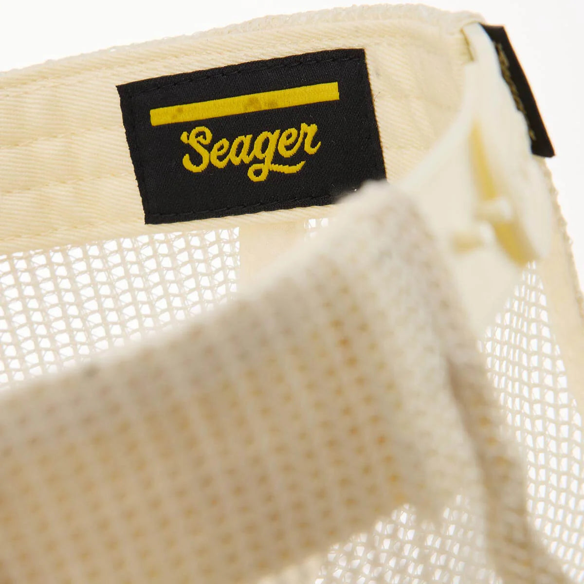 Close-up of a cream-colored mesh hat with a black and yellow Seager brand label.