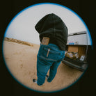 Person wearing a hoodie and jeans with a mag pocket standing next to an open car trunk in a desert setting