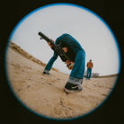 Person in a desert-like environment holding a large object, with another person in the background.