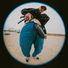 Person holding a rifle in an open field with a building in the background