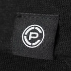 Close-up of a black knit fabric shirt featuring a square black fabric patch with a white embroidered circular logo containing a stylized letter CP.