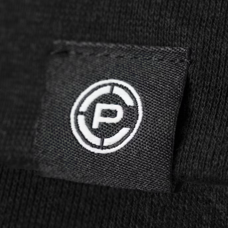 Close-up of a black knit fabric shirt featuring a square black fabric patch with a white embroidered circular logo containing a stylized letter CP.