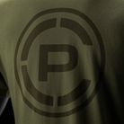 Close-up of an olive green t-shirt featuring a large, tonal dark brown circular 'CP' logo on the chest.